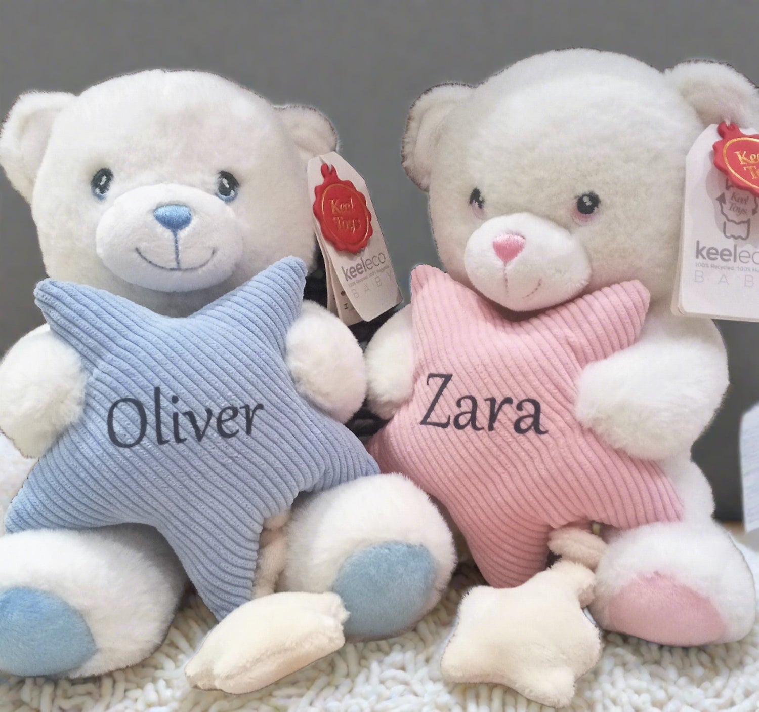 Two plush teddy bears with embroidered eyes, sitting close by each other, one holding a pastel star, both with a 'Keel-eco' brand tag.