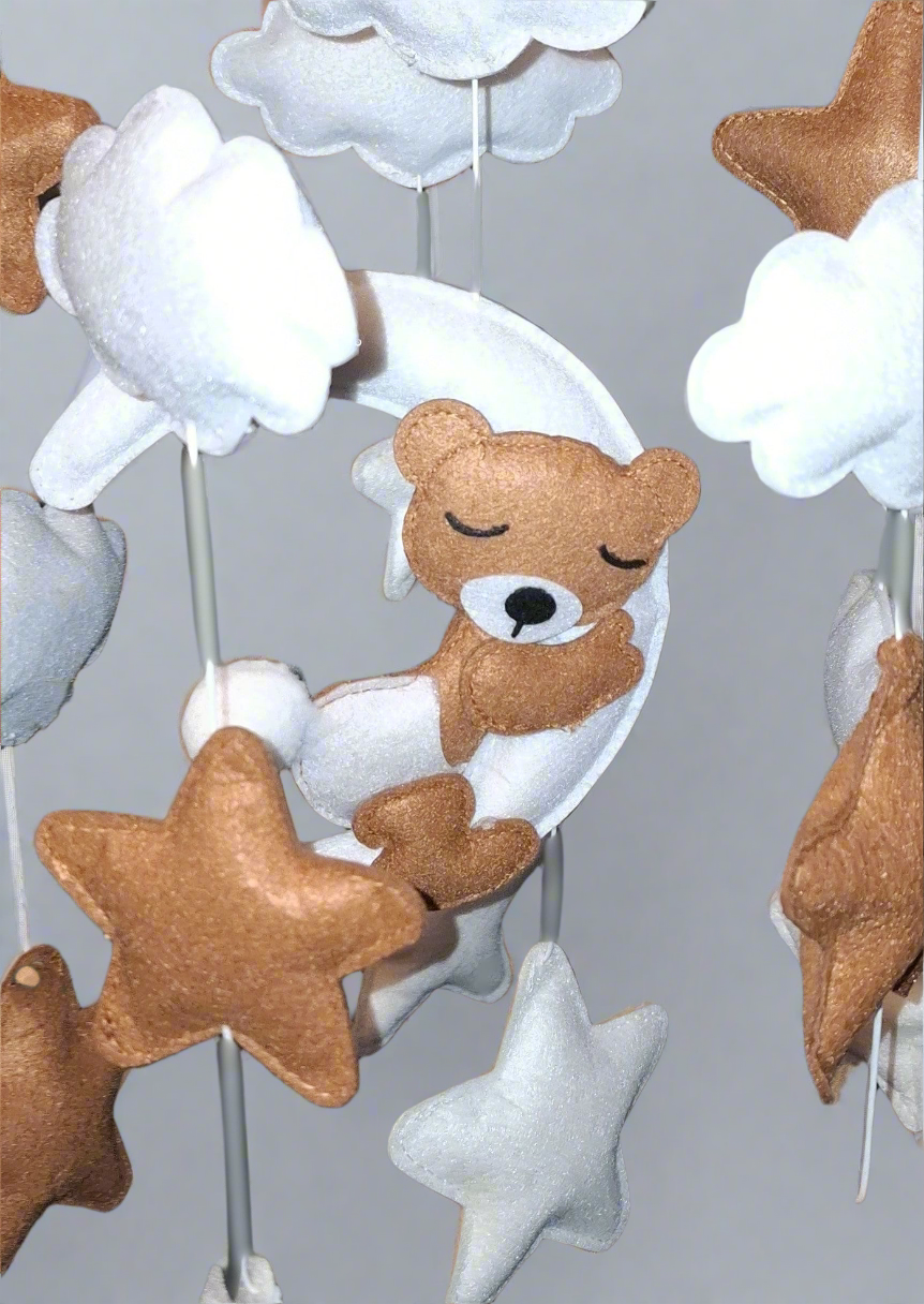 Close-up of felt teddy bear sleeping on crescent moon with cloud details